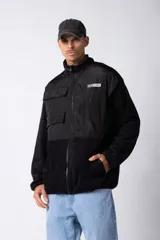 Campera negra con la parte superior de tela tipo rompevientos con dos bolsillos con solapa y la parte inferior de micro polar. Tiene cierre frontal y cuello alto.