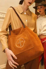 Bolso tipo tote bag de gamuza azul con asas de cuero marrón y bolsillo externo con logo bordado.