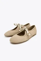 Zapato plano tipo bailarina color beige, de serraje, con puntera redondeada, suela plana y cierre con cordones.