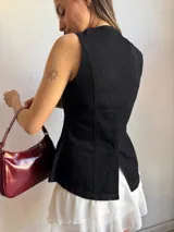Chaleco negro de denim con corte peplum, cuello redondo y cierre frontal con botones dorados.