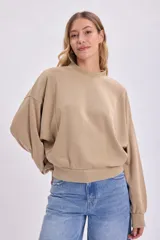 Buzo color beige de corte holgado, con cuello redondo y mangas abullonadas.