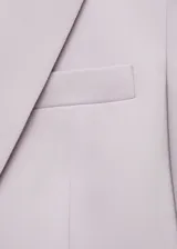 Blazer lila con solapas de muesca, hombros estructurados, cierre frontal con un botón, dos bolsillos de ribete delanteros y un bolsillo de ribete en el pecho. Tiene forro interior y abertura posterior. Diseño entallado.