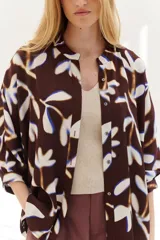 Camisa marrón con estampado de hojas blancas y azules, corte holgado, cuello mao, manga 3/4 y cierre frontal con botones.