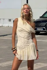 Vestido corto color crema, con escote asimétrico, detalle de bordado floral en el torso y falda con volados.