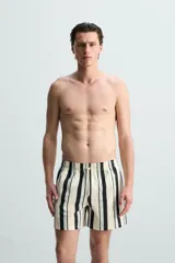 Bañador de hombre confeccionado en tejido técnico, color blanco con rayas verticales negras y celestes. Cuenta con cintura elástica ajustable con cordón, bolsillos laterales, bolsillo trasero y forro interior.