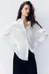 Camisa blanca de lino con cuello clásico, abotonada al frente, de manga larga con puños abotonados, canesú en la espalda, bolsillo de parche en el pecho y bajo redondeado.