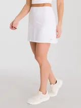 Falda deportiva blanca con calza interior, de secado rápido, corte acampanado y plisado en la parte trasera. Incluye bolsillo con cierre en la pretina y bolsillo interior en la calza.
