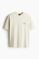 Remera color crema de corte holgado con cuello redondo y estampado pequeño con el texto "The British Museum" en el pecho.