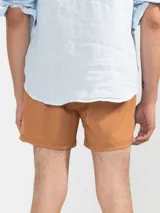 Short de baño color beige con una franja vertical marrón en el lateral. Tiene cintura elástica con cordón ajustable, bolsillos laterales y trasero con cierre, y suspensor de malla fina hipoalergénica.
