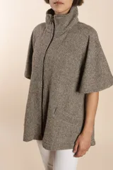 Capa acampanada color beige con manga corta, cierre metálico a la vista, cuello recto, bolsillos con tapa y terminaciones envivadas. Confeccionada en lana fina sin teñir, diseñada exclusivamente por Don Baez.