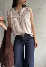 Blusa beige sin mangas con detalle de encaje en el cuello y botones en el frente.