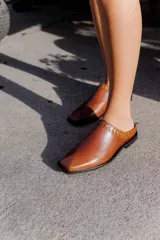 Mules de cuero negro con punta cuadrada y detalle de tachas plateadas en el borde superior.