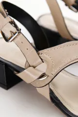 Sandalia de mujer color beige claro con taco bajo y grueso de color negro. Presenta tiras cruzadas en el empeine con un detalle de argolla metálica y tira de ajuste con hebilla en el talón.