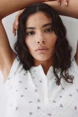 Top de manga corta en punto pointelle blanco con estampado floral diminuto en tonos rosados. Presenta cuello redondo con tapeta de botones.