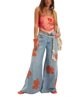 Pantalón de denim celeste de tiro medio y calce extra ancho, con flores estampadas en color naranja. Presenta bolsillos delanteros y traseros, presillas para cinturón y cierre con botón y cremallera.