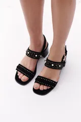 Sandalias de cuero color beige, con dos tiras horizontales sobre el empeine, una con apliques de tachas y otra con calados. Tienen pulsera con hebilla al tobillo y taco cuadrado de madera.