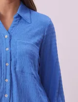 Camisa celeste de textura arrugada, con cuello clásico, cierre frontal con botones y mangas 3/4 con trabilla.