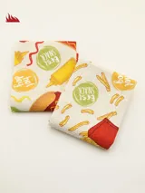 Set de dos repasadores cuadrados de tela con estampado de comida rápida: uno con papas fritas, mayonesa y ketchup, y otro con hamburguesa, mostaza y hot dog.