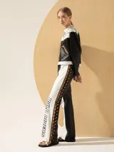 Pantalón recto de cuero blanco y negro, con detalles de cuero camel, bordados en el frente y cordones trenzados en los laterales.