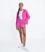 Campera rompeviento alargada color fucsia, con capucha, cierre frontal con cremallera color lila, bolsillos con solapa y puños elásticos.
