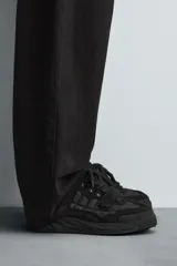 Zapatilla estilo skate de diseño robusto, confeccionada en una combinación de piezas de gamuza y material textil acolchado. Presenta un sistema de cierre con cordones gruesos y una tira de velcro en el empeine, junto con una suela de plataforma con relieve irregular.