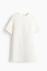 Vestido corto color blanco, de corte recto y manga corta. Presenta costuras verticales en el frente y cierre oculto en la espalda.