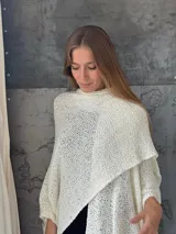Ruana color crudo tejida a mano con hilo, de diseño asimétrico y calado.