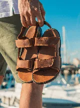 Sandalias de cuero color marrón con tiras ajustables con velcro y suela de goma negra.