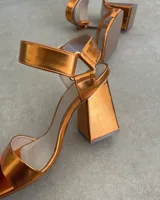 Sandalias plateadas con tira delantera, tobillera con hebilla y taco geométrico.