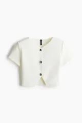 Saco corto color blanco hueso, de punto elástico con textura. Tiene cuello en V, mangas cortas, cierre frontal con tres botones grandes y abertura en el bajo.