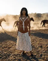 Falda midi de lino y algodón, color blanco roto con estampado de lunares marrones. Presenta un corte acampanado y un detalle de encaje blanco en la unión con la parte superior (que parece ser un top o parte de un conjunto).