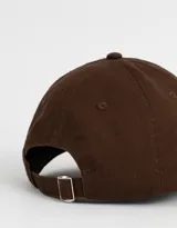 Gorra de béisbol marrón con bordado frontal de la leyenda "New York" en blanco. Presenta detalles de roturas en la visera y la corona.