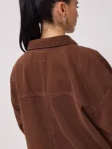Campera marrón de algodón con cuello camisero, cierre con botones a presión, bolsillos frontales y corte holgado.