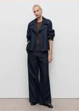 Campera corta de algodón estilo denim, color azul oscuro, con cuello solapado, cierre frontal, trabillas en los hombros y puños, y cinturón tipo batín. Presenta costuras contrastantes y un calce oversize.