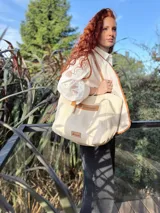 Bolso tipo tote color crema, con detalles en cuero color marrón. Tiene un bolsillo con cierre en la parte superior y un parche de cuero con el logo de la marca en la parte inferior.