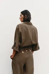 Camisa marrón de cuello solapa y manga corta con trabilla y botón. Tiene bolsillos delanteros de plastrón con solapa, bajo elástico y cierre frontal con botones a presión.