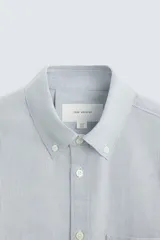 Camisa celeste a rayas verticales, de corte regular fit, confeccionada en tejido de algodón. Tiene cuello abotonado, manga larga con puños abotonados, bolsillo de parche en el pecho y cierre frontal con botones.