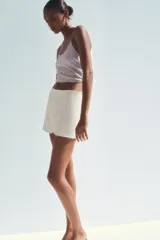 Falda pantalón corta color crema, de tiro medio con abertura en el delantero y cierre lateral con cremallera.