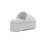 Sandalia tipo mule de plataforma blanca, con tira ancha superior adornada con tachas metálicas plateadas. La suela presenta un borde dentado.