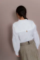 Camisa negra de lino con cuello mao, acceso frontal con botones escondidos, mangas largas abullonadas con puños color beige y botones dorados.