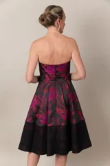 Vestido strapless negro con estampado en fucsia, con falda amplia y guarda calada en el bajo.