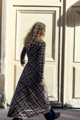 Vestido largo tipo camisero con estampado de cuadros en tonos marrón, negro y blanco. Tiene cuello solapa, mangas largas con puños abotonados, dos bolsillos de parche con solapa en el pecho y cierre frontal con botones a presión.
