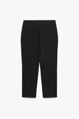 Pantalón negro tobillero de tiro alto con bolsillos delanteros y traseros. Tiene abertura lateral en el bajo y cierre frontal con cremallera y botón.