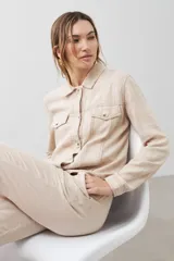 Chaqueta color beige melange de lino con pespuntes a contraste, cuello camisero, cierre frontal con botones, bolsillos de parche en el pecho y corte recto.
