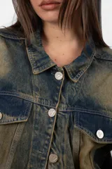 Campera de jean azul con lavado matizado, corte regular, acceso con botones personalizados, bolsillos delanteros con tapa y bolsillos laterales funcionales. Cada prenda es elaborada de manera artesanal, lo que las distingue unas de otras. Los tonos en el lavado pueden variar desde claros hasta oscuros.