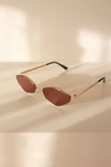 Lentes de sol con montura metálica dorada y cristales de forma geométrica (diamante/hexagonal) en tono marrón. Las patillas son doradas con puntas negras.