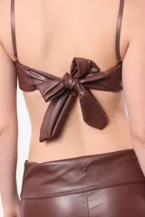 Top brasier color marrón de cuerina elastizada, con aro media copa en busto, breteles regulables y acceso por espalda mediante lazo.