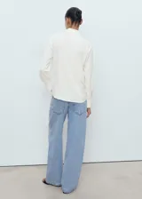 Camisa blanca de manga larga con puños abotonados, cuello camisero y cierre frontal de botones. Diseño recto con tejido fluido.