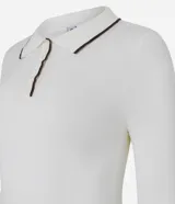 Blusa blanca de punto con cuello polo y mangas largas. Presenta detalles contrastantes en negro en el cuello, la abertura frontal y el dobladillo.