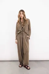 Pantalón de lino color marrón, de tiro medio con elástico y lazo en la cintura, puño en el tobillo con botón de nácar.